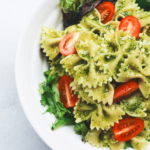 A white bowl of bowtie pesto pasta salad