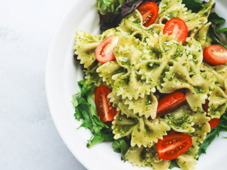 A white bowl of bowtie pesto pasta salad