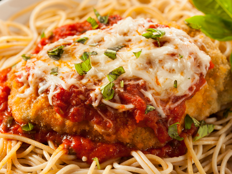 Chicken coated in breadcrumbs with tomato sauce and parmesan cheese melted on top over spaghetti noodles
