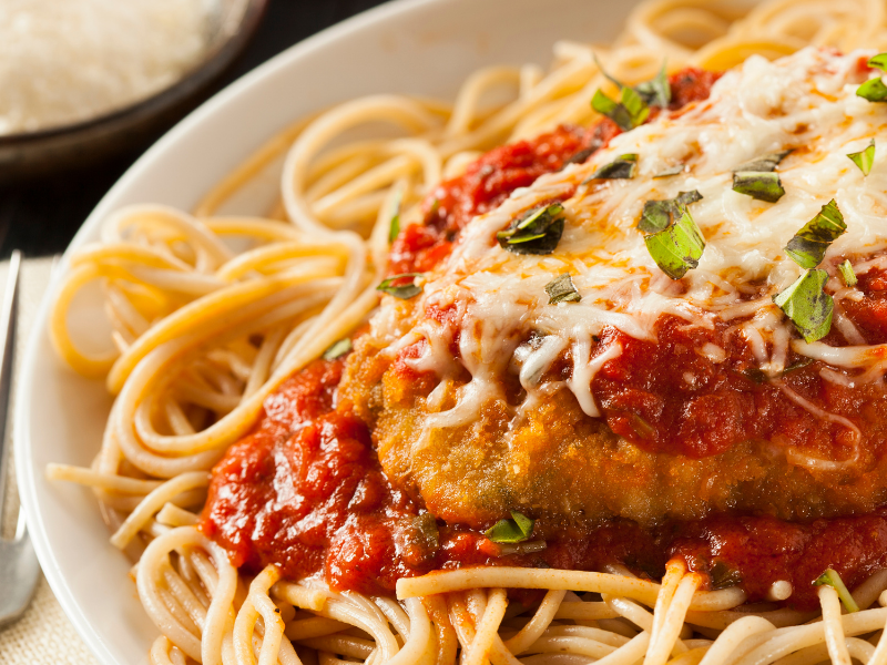 Chicken parmesan in a white plate coated in breadcrumbs with tomato sauce and parmesan cheese melted on top over spaghetti noodles