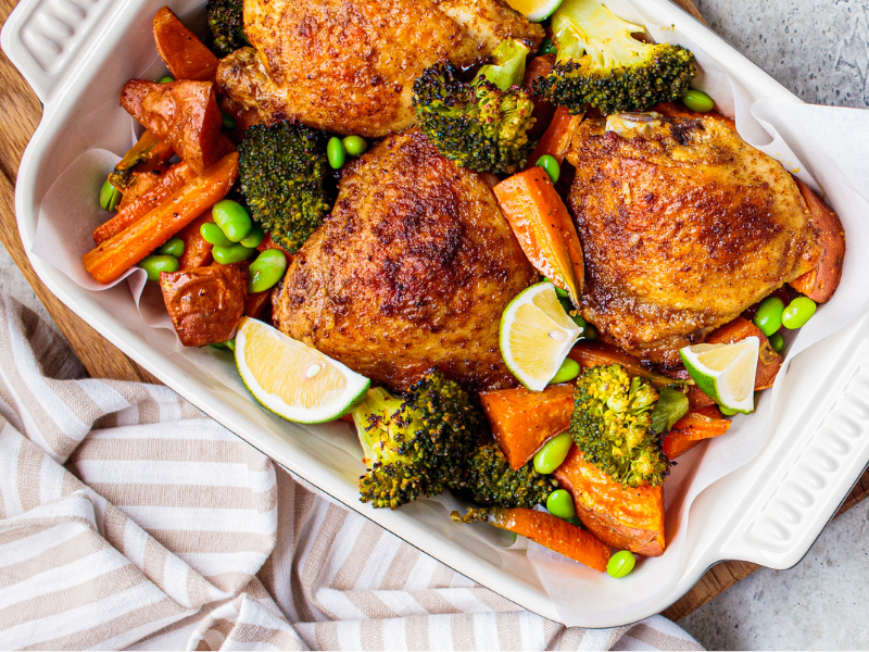 Oven baked, roasted chicken thighs with broccoli, carrots, edamame in a white dish
