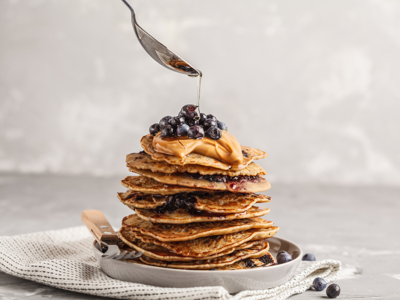 Vegan peanut butter blueberry pancakes with a spoon pouring syrup